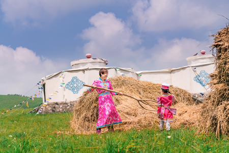 Mongolian mother and daughter working in front of the grassの写真素材