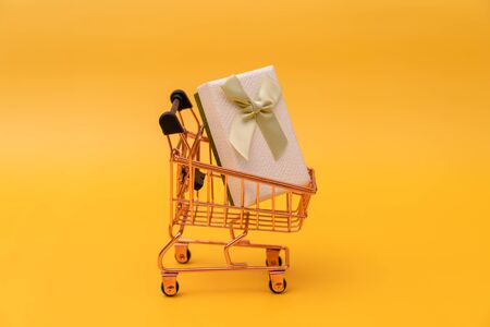 Shopping cart and gift box on yellow backgroundの写真素材
