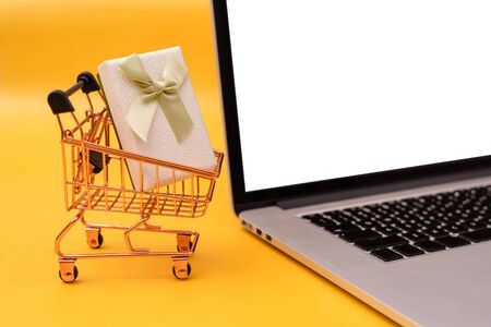 Shopping cart, laptop and gift box on yellow backgroundの写真素材