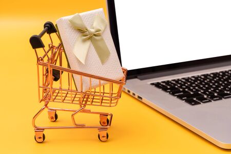 Shopping cart, laptop and gift box on yellow backgroundの写真素材