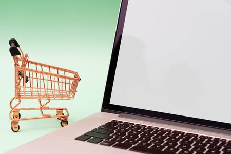 Laptop and shopping cart on green backgroundの写真素材