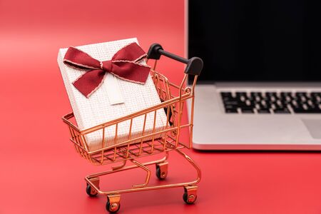 Laptop and shopping cart with gift on red backgroundの写真素材