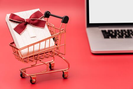 Laptop and shopping cart with gift on red backgroundの写真素材