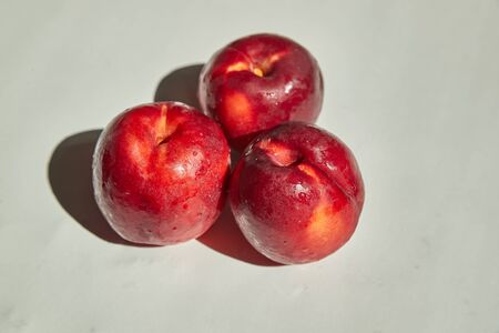 Three beautiful ripe, juicy nectarines lie on a white tableの写真素材