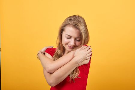 young blonde girl in red t-shirt over isolated orange background shows emotions