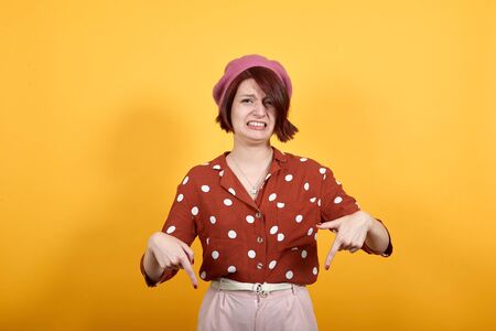 Young beautiful woman wearing red shirt with white polka dot standing over yellow isolated...