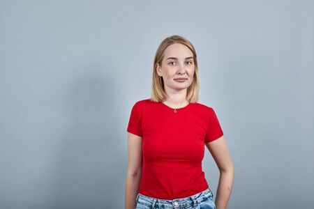 Young sad frustrated worried unshaven woman in red shirt looking camera isolated on gray wall background studio portrait. People sincere emotions lifestyle concept.の写真素材