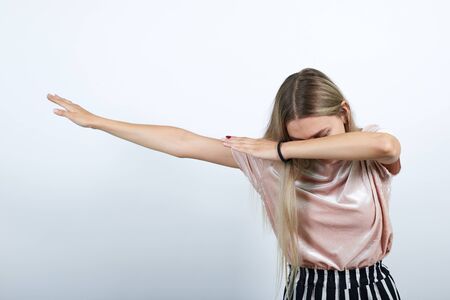 Young teen woman in pastel pink shirt doing dab dance gesture with hands isolated on white wall background, studio portrait. People lifestyle concept.の写真素材
