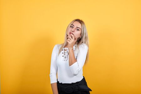 Portrait of cute smiling young woman in pastel white shirt hand prop up on mouth, isolated on orange wall background in studio. People sincere emotions, lifestyle concept.の写真素材