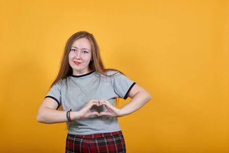 Young attractive caucasian woman in nice clothes showing shape heart with hands, isolated on orange...