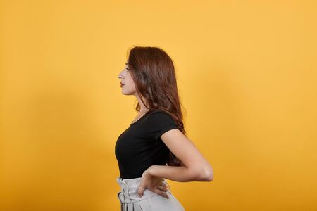 Beautiful girl in black is posing for some photo shot in studie near yellow wall.