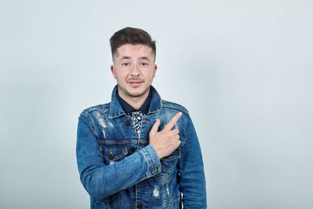 Beautiful caucasian young funny man wearing casual denim jacket on isolated gray background looking serious and keeping finger asideの写真素材