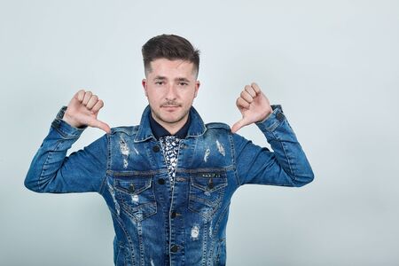 Handsome caucasian young man over isolated gray wall wearing fashion clothes pointing thumbs on...
