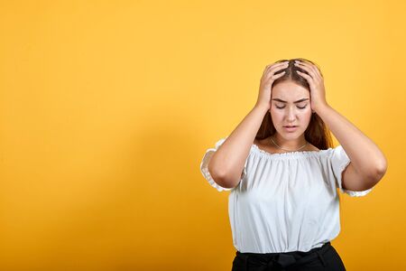 Sick young woman keeping hand on head, headache isolated on orange background in studio in casual white shirt. People sincere emotions, lifestyle concept.の写真素材