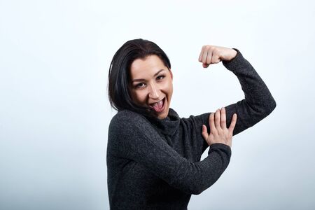 Strong caucasian young woman in fashion black sweater over isolated white background, showing muscles, keeping hand on it. Lifestyle conceptの写真素材