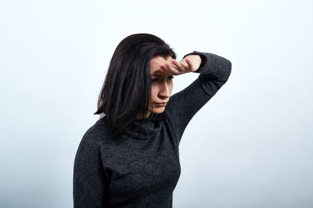 Caucasian young woman in fashion black sweater keeping hand on forehead, looking into distance over isolated white background, Lifestyle conceptの写真素材