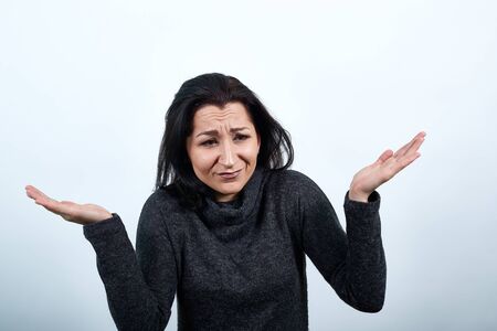 Disappointed caucasian young woman in fashion black sweater spreads hands, looking unhappy over isolated white background, Lifestyle conceptの写真素材