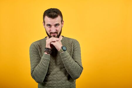 Young handsome caucasian man over isolated orange background looking at camera, keeping hand on chin...