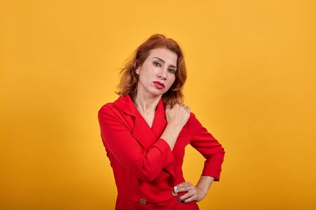 Unhappy caucasian young woman wearing fashion red jacket over isolated orange background keeping hand on back, pain in muscules, holding hand on belt. People lifestyle concept.の写真素材