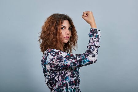 Serious charming young lady over isolated gray background in fashion shirt staying sideways, keeping...