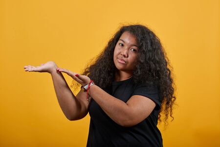 Disappointed young woman with overweight pointing hands aside, looking at camera over isolated orange background wearing fashion black shirt. People lifestyle concepte.の写真素材