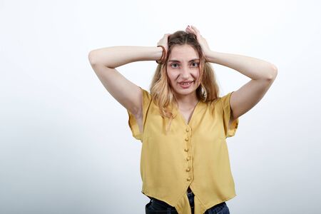 Cheerful woman keeping hand on head, smiling wearing fashion yellow shirt isolated on white background in studio. People sincere emotions, lifestyle concept.の写真素材