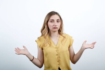 Disappointed woman spreads hand at camera, unhappy wearing fashion yellow shirt isolated on white background in studio. People sincere emotions, lifestyle concept.の写真素材
