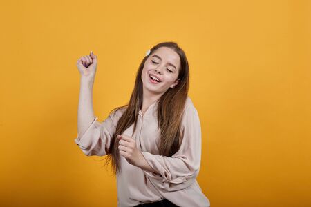 Cheerful caucasian brunette woman in fashion pastel shirt, dancing, keeping fist aside, enjoying isolated on orange background in studio. People sincere emotions, lifestyle concept.の写真素材