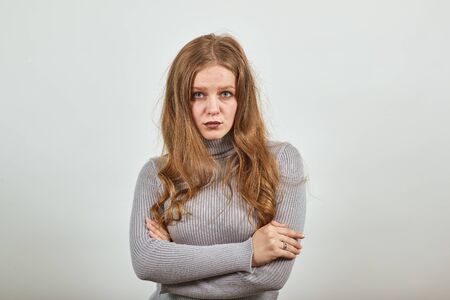 a young beautiful red haired woman in gray sweater cool look has hands crossed and is looking