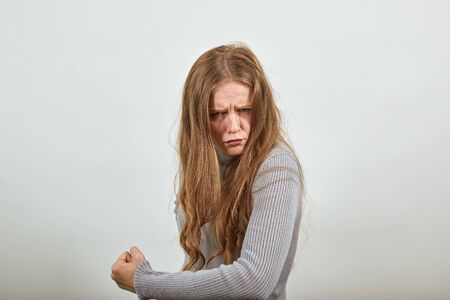 A young beautiful red-haired woman in gray sweater with an evil look shows anger, stubbornness, hatred, shows fistの写真素材