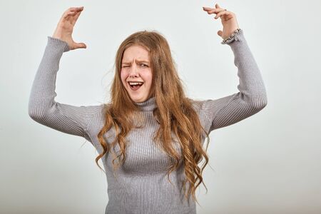 A young beautiful red haired woman in gray sweater happily raises her hands and screams with...