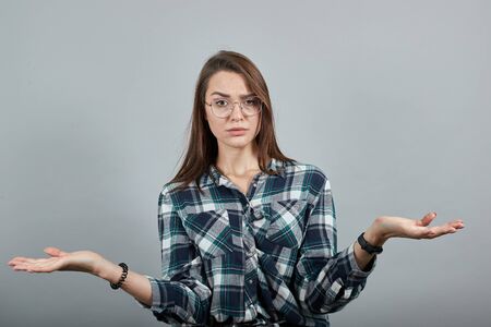 Young brunette girl blue green in checked shirt on grey background shocked woman spreads her hands