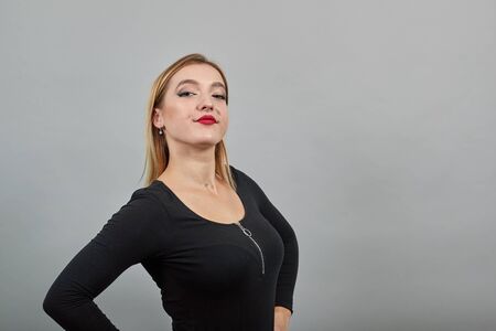 Young blonde girl in black jacket on grey background satisfied woman posing on camera
