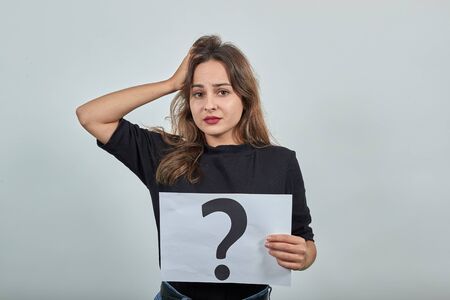 Cute Young Brunette Woman In Black T-Shirt, Blue Jeans With Belt On Gray Background, Confused Girl...