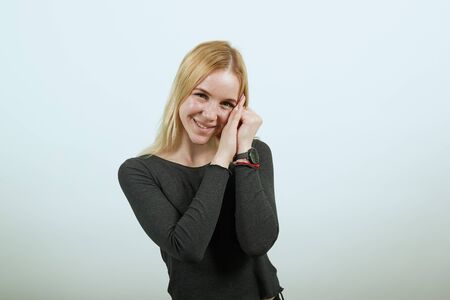 Young Blonde Woman In Black Sweater With Stylish Watch On White Background, Cute Girl Holds Hands Together Near Her Face, Looks Friendly With Love. The Concept Innocence And Tenderness Of Peopleの写真素材