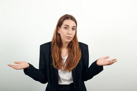 Palms up, place your product here, raising arms wide spread is catching something. Young attractive woman with brown hair in a light t-shirt and black jacket on white backgroundの写真素材