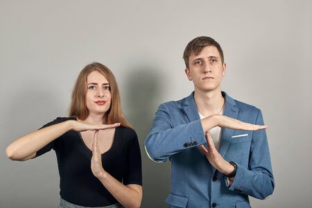 Time out gesture, break, doing t symbol or sign with help of hands. Young attractive couple boyfriend girlfriend two people, dressed black t-shirt, blue jacket, grey backgroundの写真素材