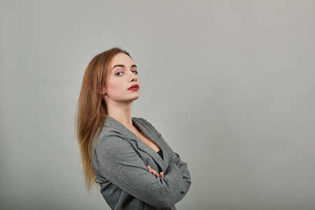 Standing and cross her arms on chest. Young attractive woman, dressed gray jacket, with green eyes,...