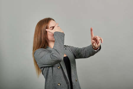 Closing face palms covers eyes visible through with hands. Young attractive woman, dressed gray jacket, with green eyes, light brown hair, backgroundの写真素材