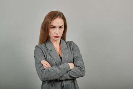Standing and cross her arms on chest. Young attractive woman, dressed gray jacket, with green eyes, light brown hair, backgroundの写真素材