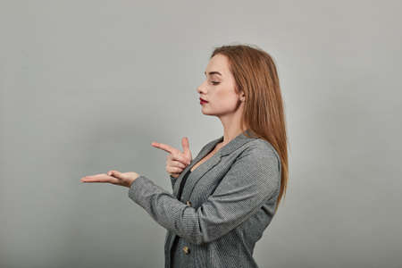 Palms up, place your product here, raising arms wide spread is catching something. Young attractive woman, dressed gray jacket, with green eyes, light brown hair, backgroundの写真素材