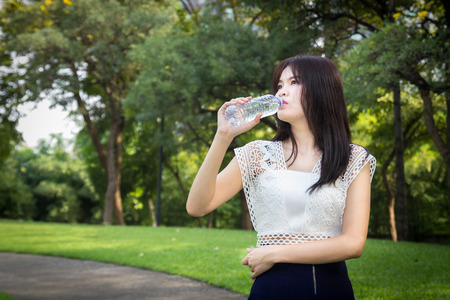Photo of Young beautiful  woman wearing white shirts drinking water at summer green parkの写真素材