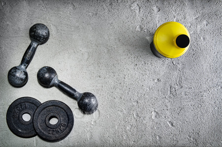 Fitness or bodybuilding concept background. Product photograph of old iron dumbbells and shaker on grey, conrete floor in the gym. Photograph taken from above, top view with lots of copy spaceの写真素材