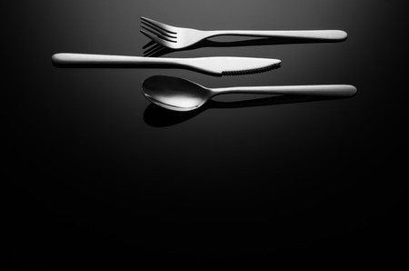 Black food background. Stainless steel, modern silverware on black background with reflection. Image...