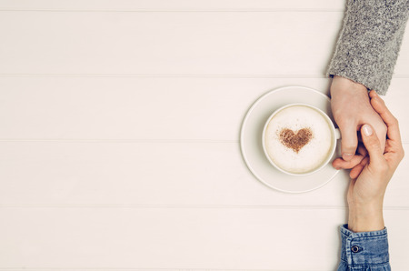 Couple in love holding hands with coffee on white wooden table. Photograph taken from above, top view with copy spaceの写真素材
