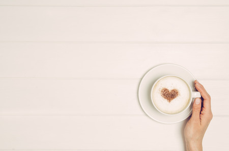 Female hand holding cup of coffee on white wooden table. Photograph taken from above, top view with copy spaceの写真素材