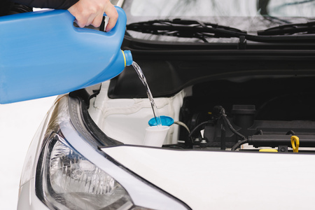 Car maintenance. Man pouring car winter windshield washer fluid outdoor. Closeup image taken outdoors.の写真素材