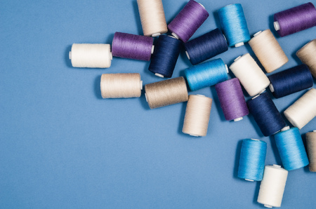 Top view of colorful thread spools over blue seamless background. Image taken from above.