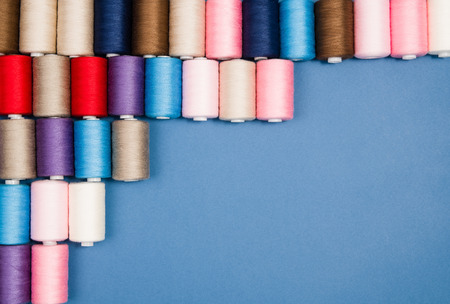 Top view of colorful thread spools over blue seamless background. Image taken from above.