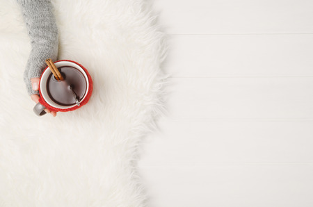 Female hand holding a cup of tea or coffee on white wooden table. Winter or christmas cosy background. Photograph taken from above, top view with copy spaceの写真素材